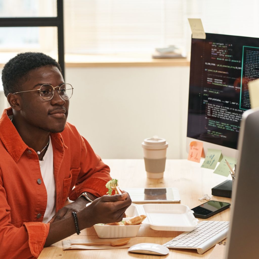 Young African American IT engineer looking at computer screen by lunch
